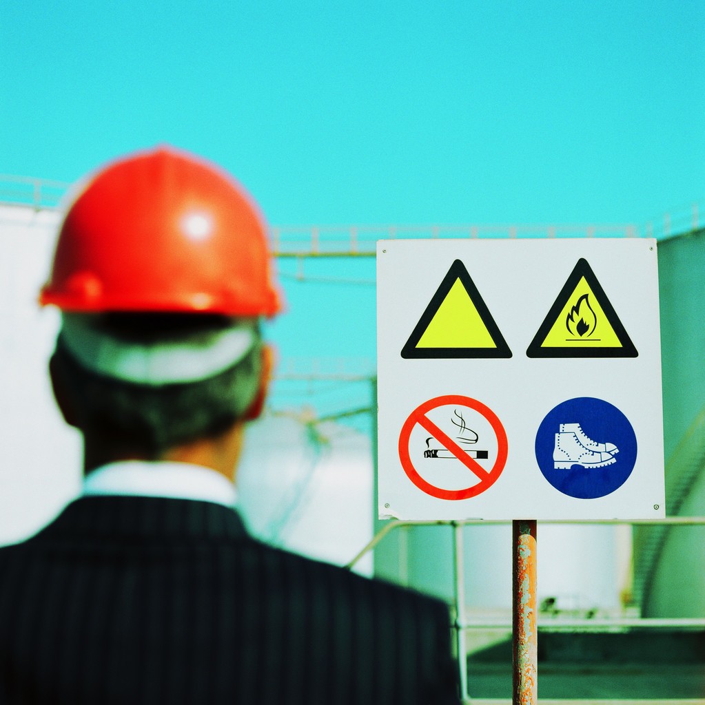 Businessman Wearing a Hard-Hat Looking at a Hazard Sign --- Image by © Royalty-Free/Corbis